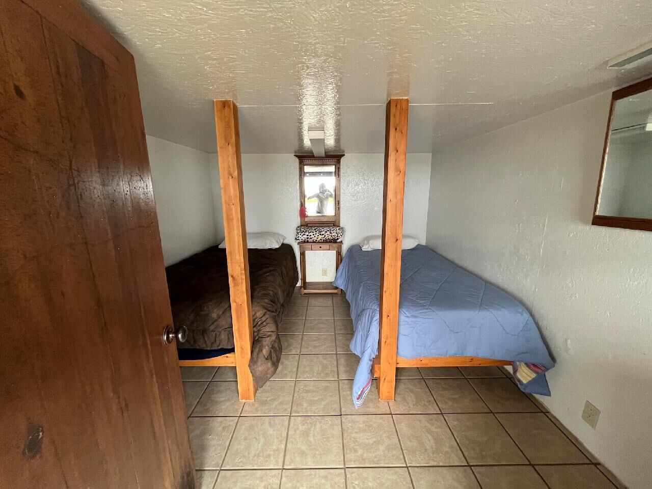 A small room with two wooden bunk beds, a small table with a chair, and a window.