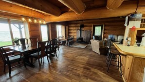 Interior de una cabaña de madera con comedor, chimenea y barra.