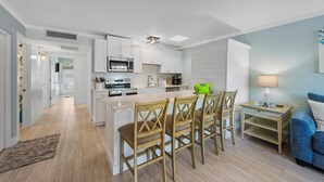 Une cuisine moderne avec des meubles blancs, un îlot central doté de chaises, un four à micro-ondes et une machine à café.
