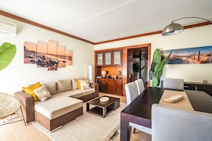 A modern living room with a sectional sofa, a dining table, and a kitchen area in the background.