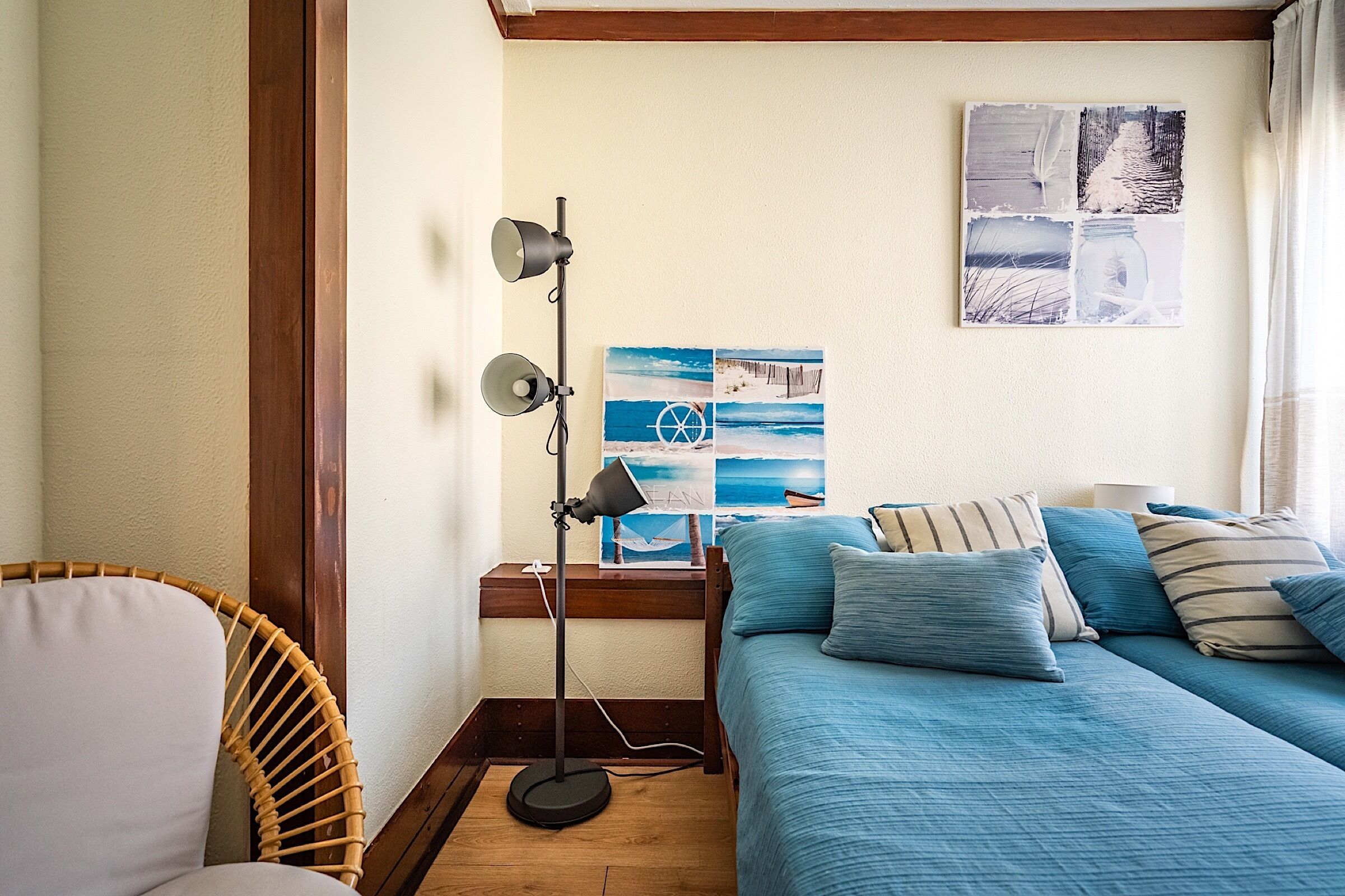 A bedroom with a bed, a standing lamp, a wicker chair, and a wall art piece.