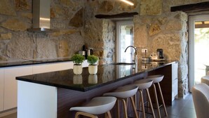 A modern kitchen with a stone wall, a large island with bar stools, and a built-in oven. - Casa do Sobreiro / Casas de Basto (Infesta)
