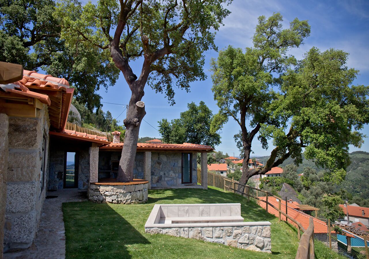 A stone building with a tiled roof, a stone bench, and a grassy area.