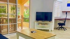 Un salon avec une télévision, une table en bois, un canapé et un balcon agrémenté de plantes.