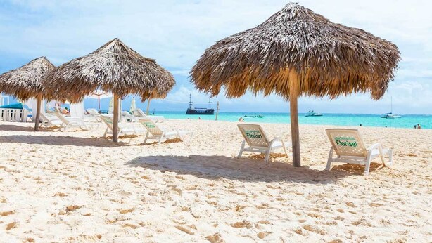 Une plage avec des parasols en chaume et des chaises longues blanches.