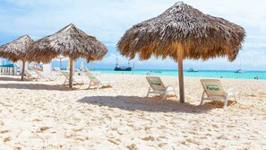 A beach with thatched umbrellas and white lounge chairs.