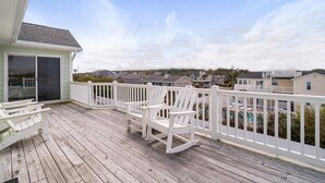 Eine Holzterrasse mit weißen Geländern, einer Schiebetür und zwei weißen Adirondack-Stühlen.