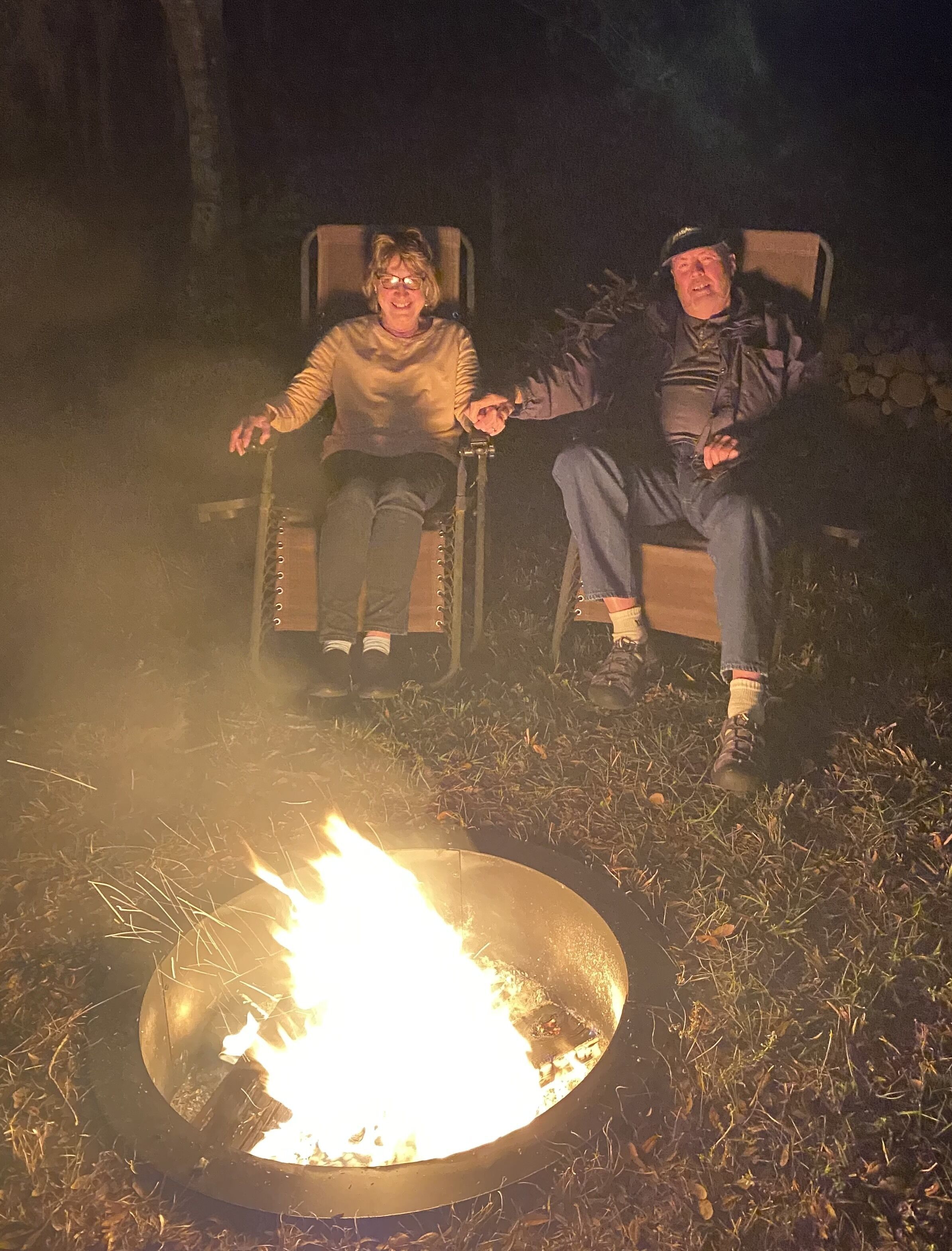 Two people sitting on chairs by a campfire.