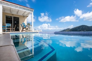 A clear blue infinity pool with a view of a mountain and a white building with blue chairs. - Awesome views, private pool, air conditioning, close to beaches, restaurants! (St John)