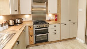 Une cuisine compacte équipée d’une cuisinière à gaz, d’un four et d’une hotte en acier inoxydable. On y trouve des armoires en bois et un plan de travail agrémenté d’appareils de cuisine.