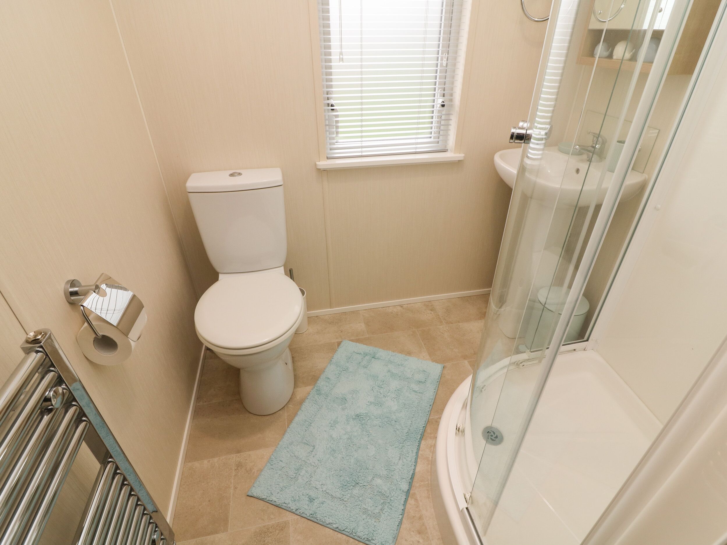A bathroom with a toilet, a glass shower enclosure, and a small window with blinds.