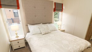 Un lit bien fait, recouvert d’une couvre-lit à motifs, une table de chevet avec une lampe et une fenêtre donnant sur l’extérieur.