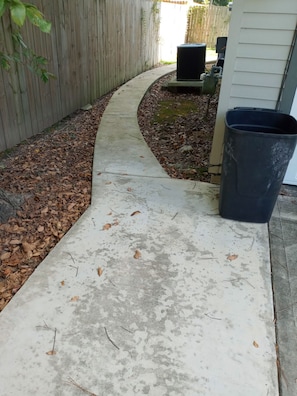 A concrete pathway with scattered leaves, a wooden fence, and a black trash bin. - Garage Guest Suite (Houston)