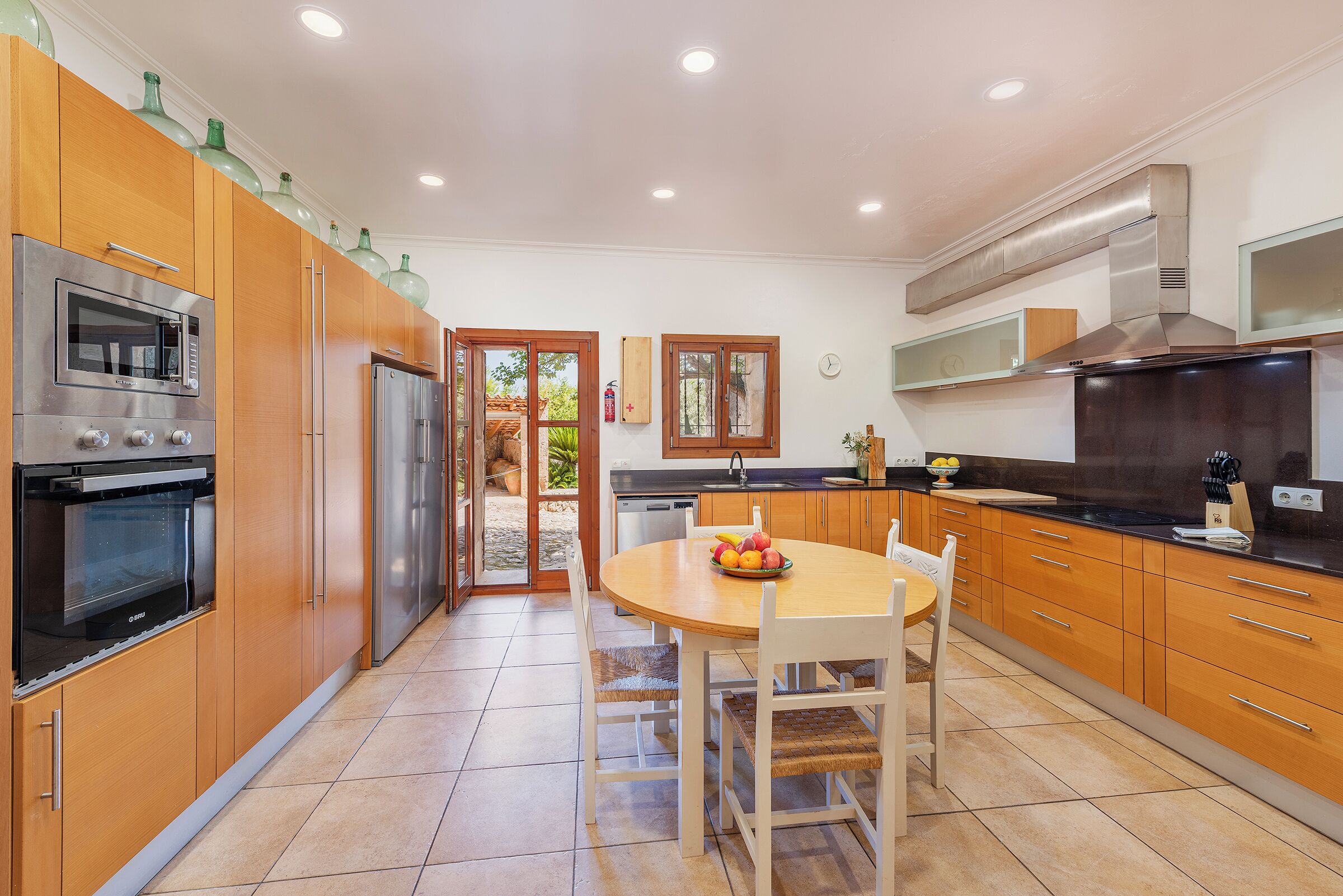 A modern kitchen with wooden cabinets, stainless steel appliances, and a dining area with a round table and chairs.