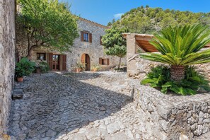 A stone building with a cobblestone courtyard, wooden shutters, and potted plants. - Villa Pontarro (Pollença)
