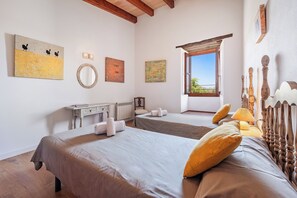 A hotel room with two beds, a wooden headboard, a window with a view, and artwork on the walls. - Villa Pontarro (Pollença)