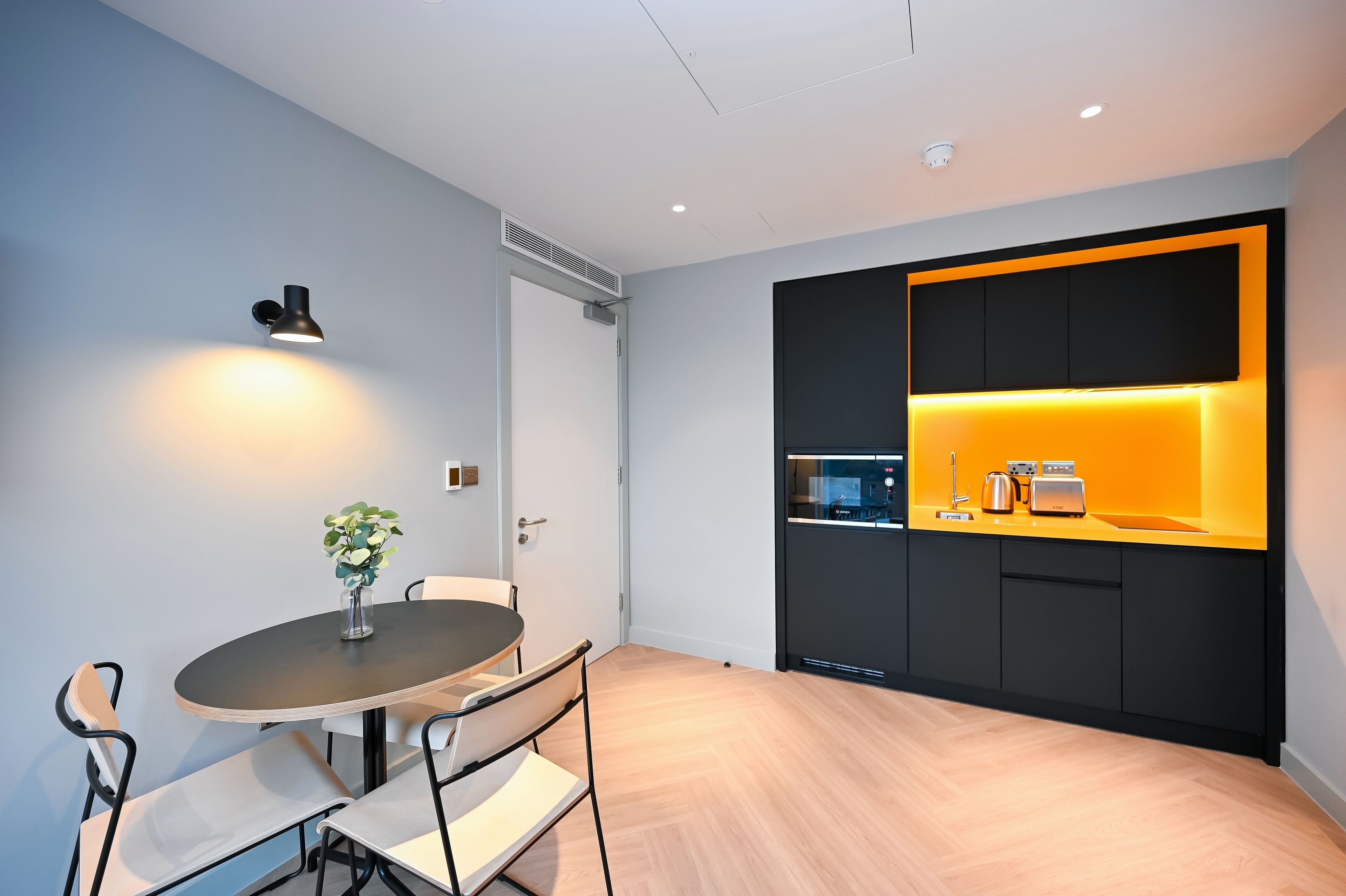 Una cocina moderna con una decoración en tonos negro y amarillo, una mesa redonda con sillas y una pequeña planta en maceta sobre la mesa.
