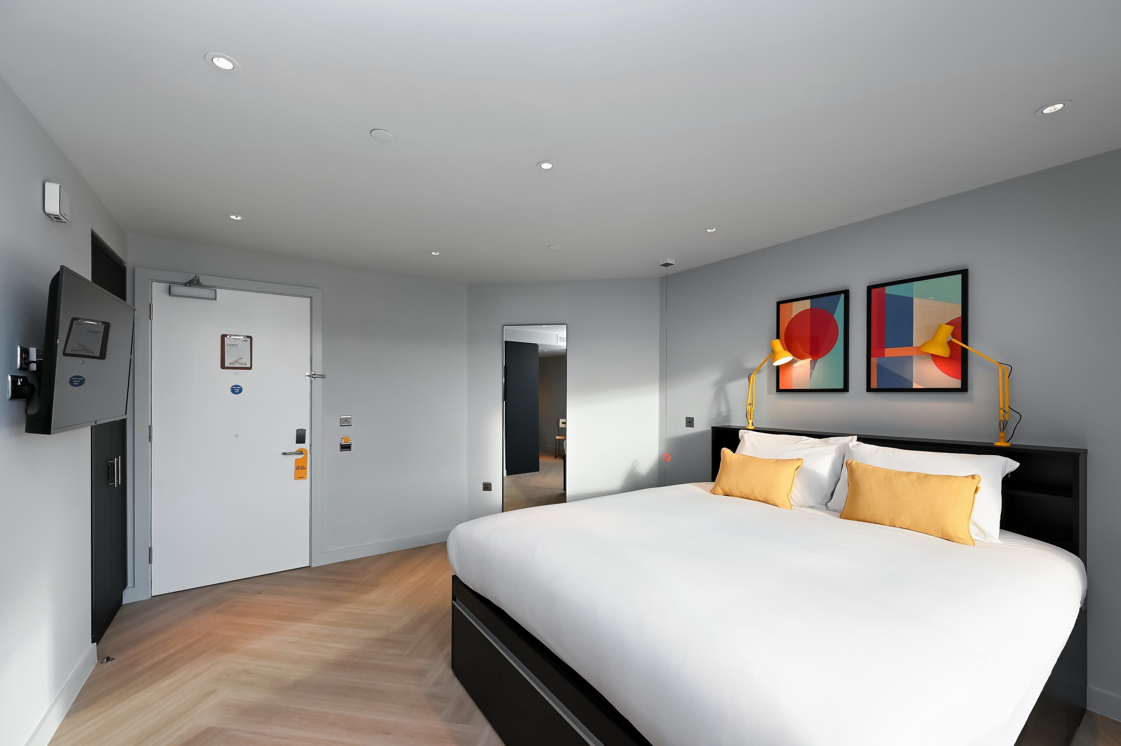 Una habitació d'hotel moderna amb un llit gran, un televisor de pantalla plana fixat a la paret i obra d'art sobre el llit.