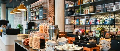 Un bufé de desayuno con diversos alimentos y recipientes, una estación de café y estanterías llenas de utensilios de cocina y provisiones.