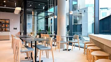 A modern cafe with tables and chairs arranged around a central area, large windows, and a visible outdoor view.