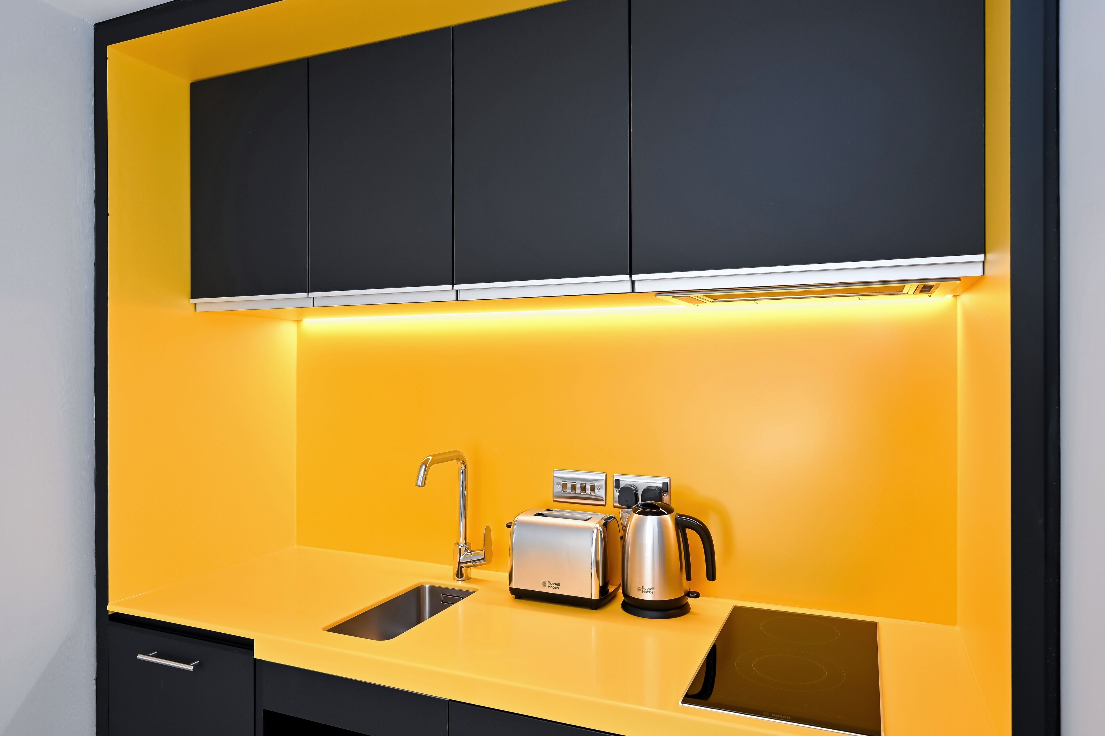 A kitchen with a yellow countertop, a sink, a toaster, and a kettle.