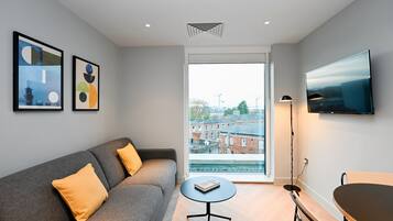 A modern living room with a grey sofa, yellow cushions, a round coffee table, a flat-screen TV, and artwork on the walls.
