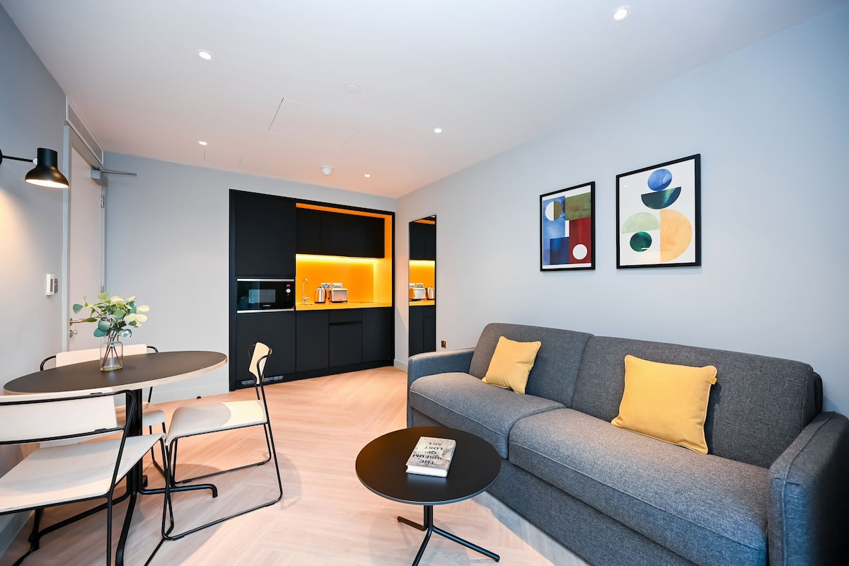 Ein modernes Wohnzimmer mit einem grauen Sofa, einem kleinen runden Couchtisch und einem Essbereich mit weißem Tisch und Stühlen.