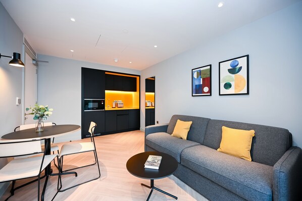 A modern living room with a grey sofa, a small round table, and a dining area with a white table and chairs. - Staycity Aparthotels, Dublin, Mark Street (Dublin)