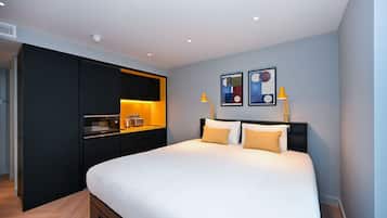 Una habitación de hotel moderna con una cama grande, un escritorio integrado y una kitchenette pequeña.