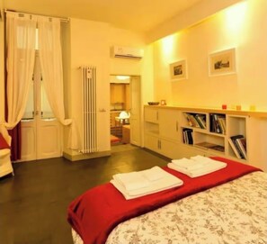 A hotel room with a bed, a desk, a chair, a radiator, a bookshelf, and a bathroom visible through a door. - Maison PANTHEON with SAUNA + Breakfast included (Roma)