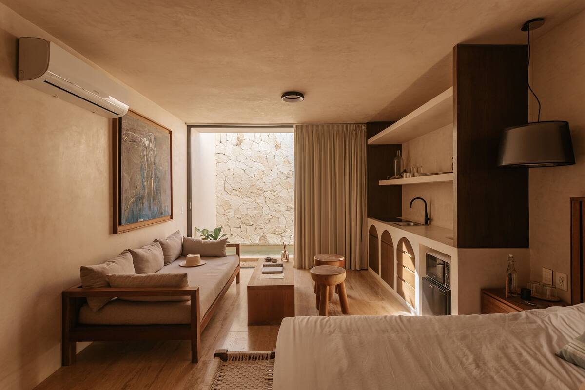 Quarto moderno com sofá, cama, mesinha e vista para uma parede de pedra.