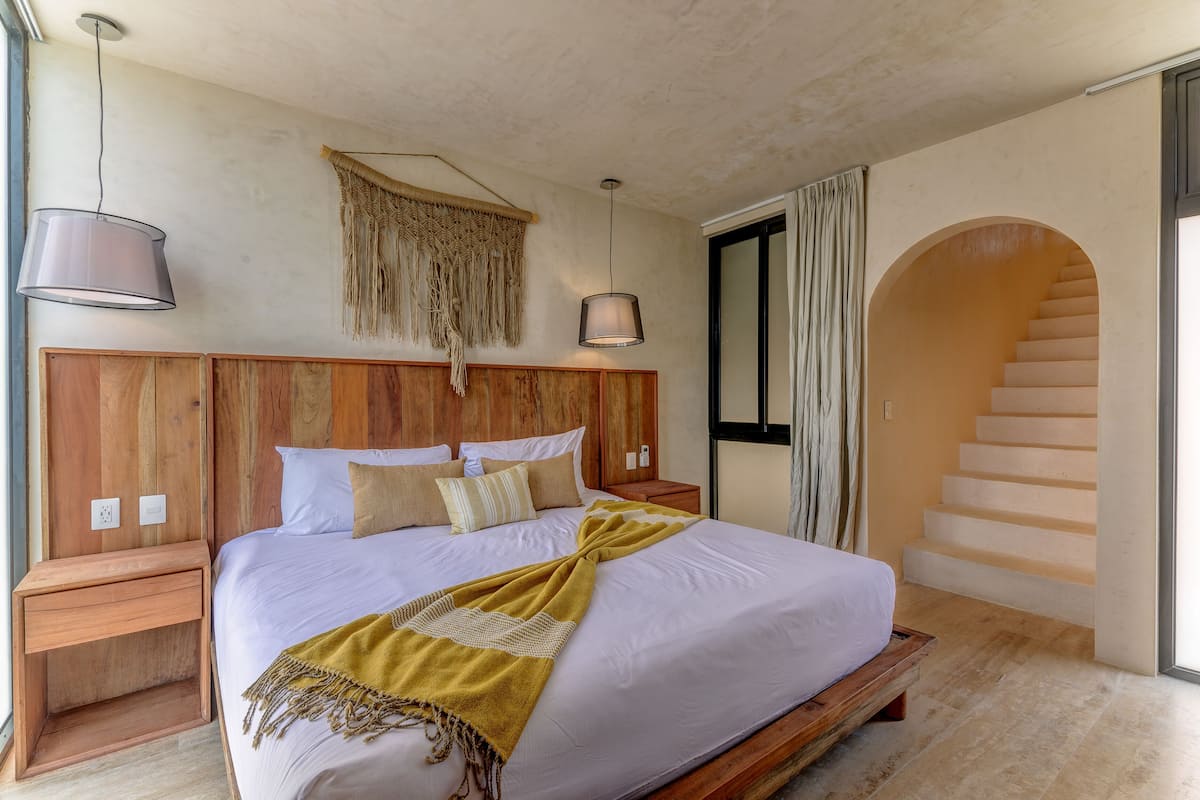 Um quarto com uma cama grande, cabeceira de madeira, mesas de cabeceira e uma escada que leva a um andar superior.
