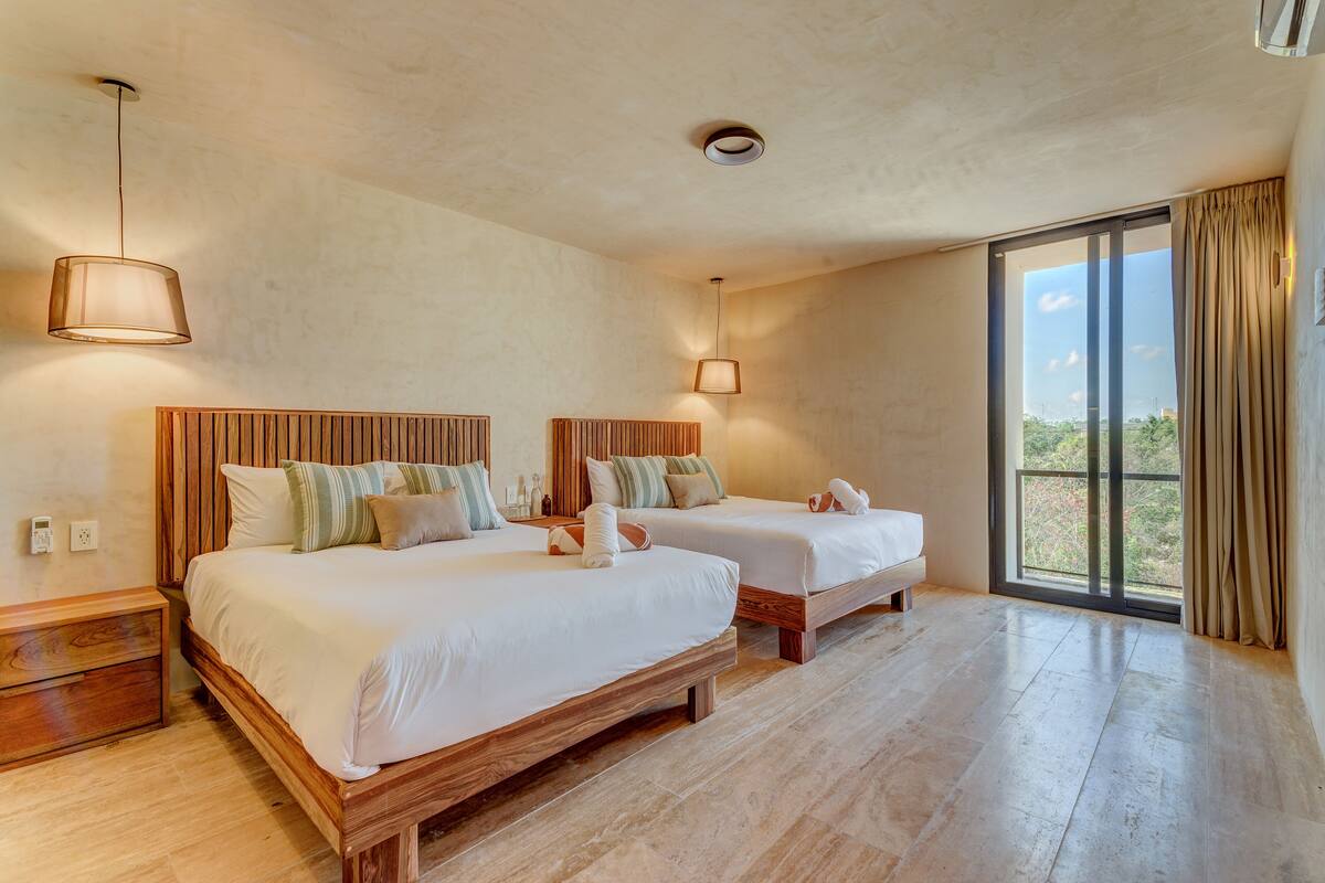 Quarto de hotel com duas camas de madeira, uma janela ampla com vista e um lustre.