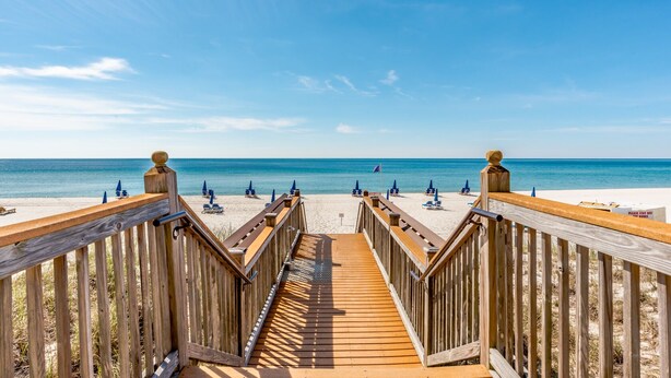 A wooden boardwalk leading to a beach with blue umbrellas and lounge chairs. - Palacio 3/2 on 17th Floor with a Million Dollar View (Pensacola)