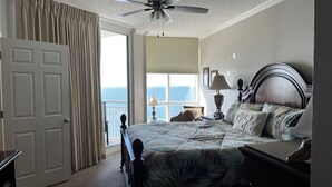 A hotel room with a bed, a nightstand, a lamp, a ceiling fan, a view of the ocean, and a door. - Palacio 3/2 on 17th Floor with a Million Dollar View (Pensacola)