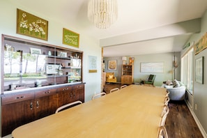 A dining area with a long wooden table, chairs, and a wooden cabinet with shelves.