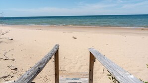Een houten trap die naar een zandstrand leidt, met helderblauw water op de achtergrond.