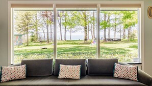 Een kamer met een groot raam dat uitkijkt op een grasrijk gebied met bomen en uitzicht op zee.