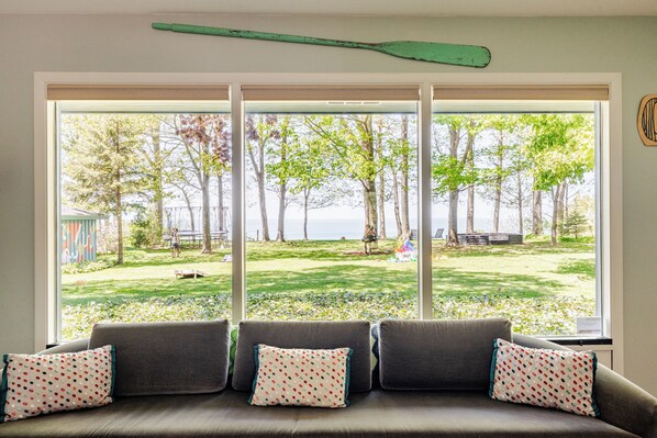 A room with a large window overlooking a grassy area with trees and a view of the sea. - All The Waters Retro Home on Lake Michigan- PRIVATE BEACH-Large, shaded backyard (Benton Harbor)