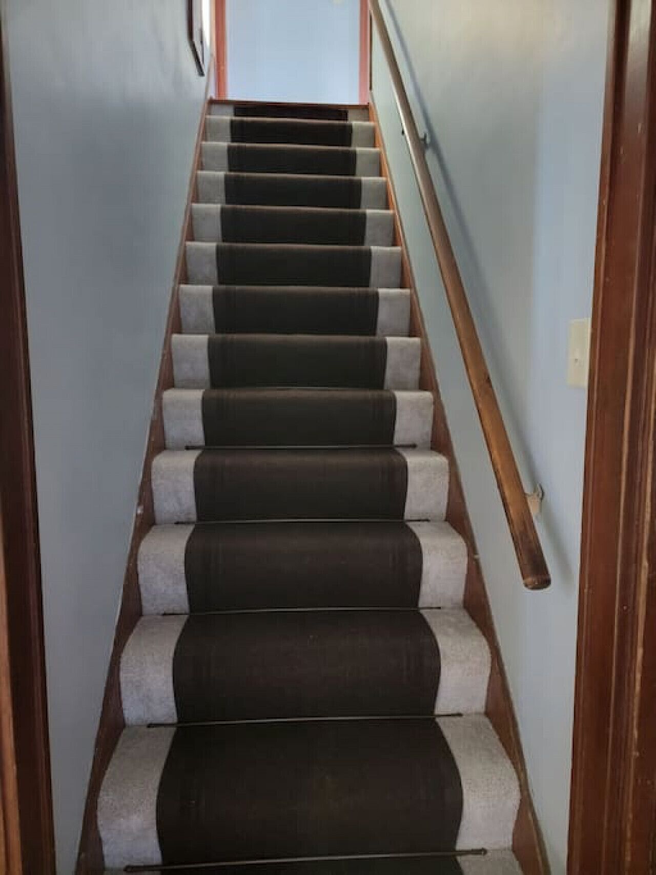 A staircase with alternating dark and light steps, wooden handrails, and a light-colored wall.