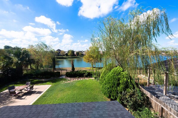 A patio with outdoor furniture, a grassy area, and a view of a lake with houses in the background.