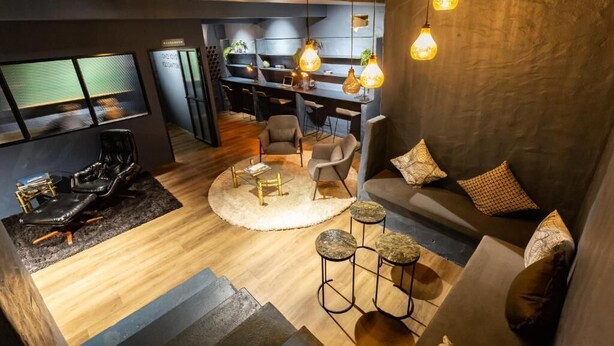 Een moderne woonkamer met een bank, salontafel en stoelen. In de achtergrond is een keuken met barstoelen.