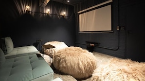 Een gezellige kamer met een comfortabele bank, een groot, bekleed voetenbankje en een projectiescherm aan de muur.
