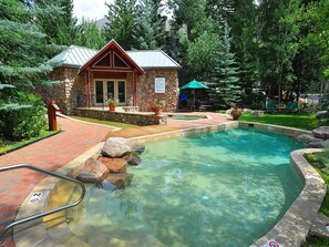 Un bâtiment en pierre doté d’une piscine, entouré d’arbres et agrémenté d’un espace patio.