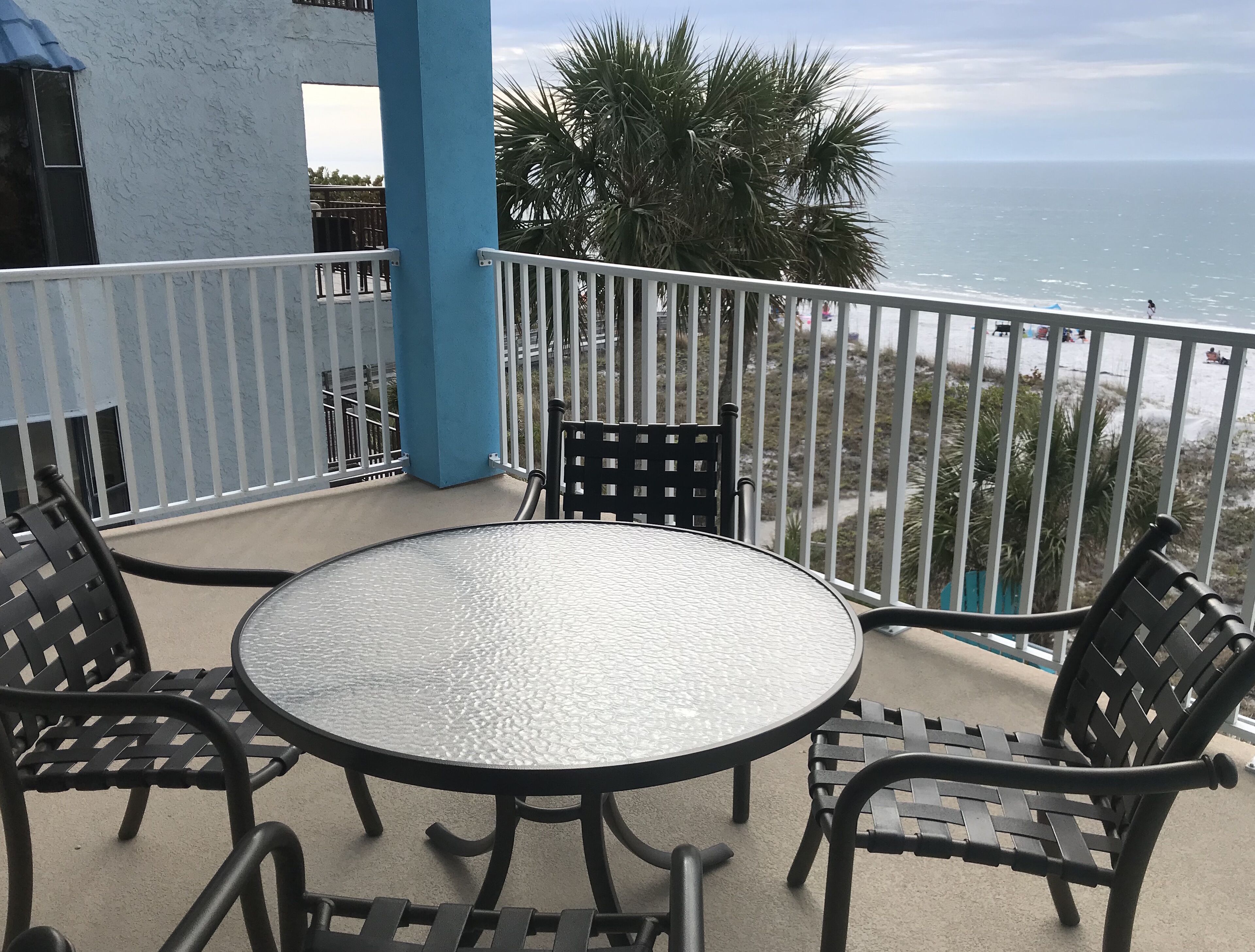 A round table with four chairs on a balcony overlooking the ocean.