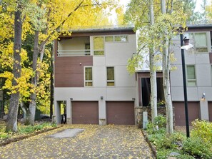 A modern two-story building with a flat roof, numbered 7B and 7D, surrounded by trees with yellow leaves.