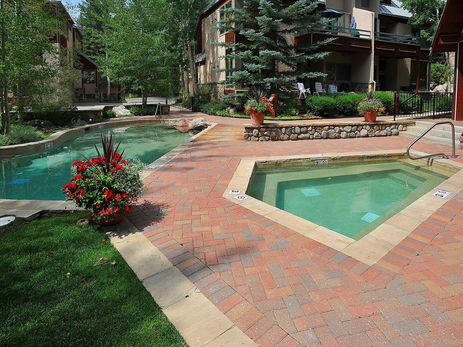A pool area with two rectangular pools, surrounded by brick pathways and greenery.