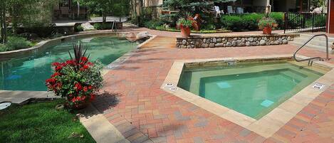 A pool area with two rectangular pools, surrounded by brick pathways and greenery.