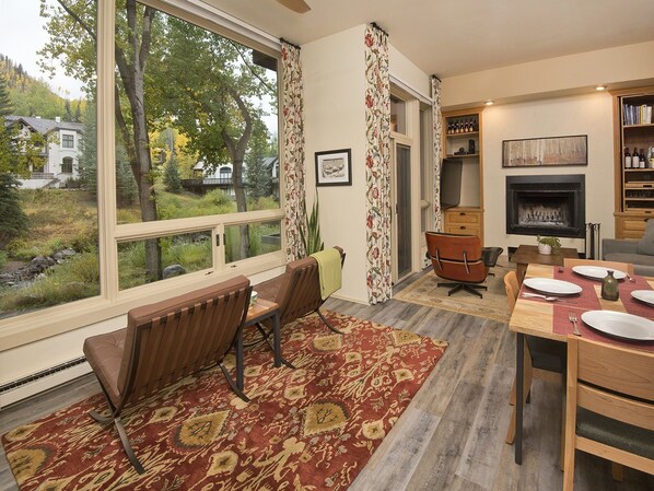 A dining area with a large window, a fireplace, and a view of the outdoors.