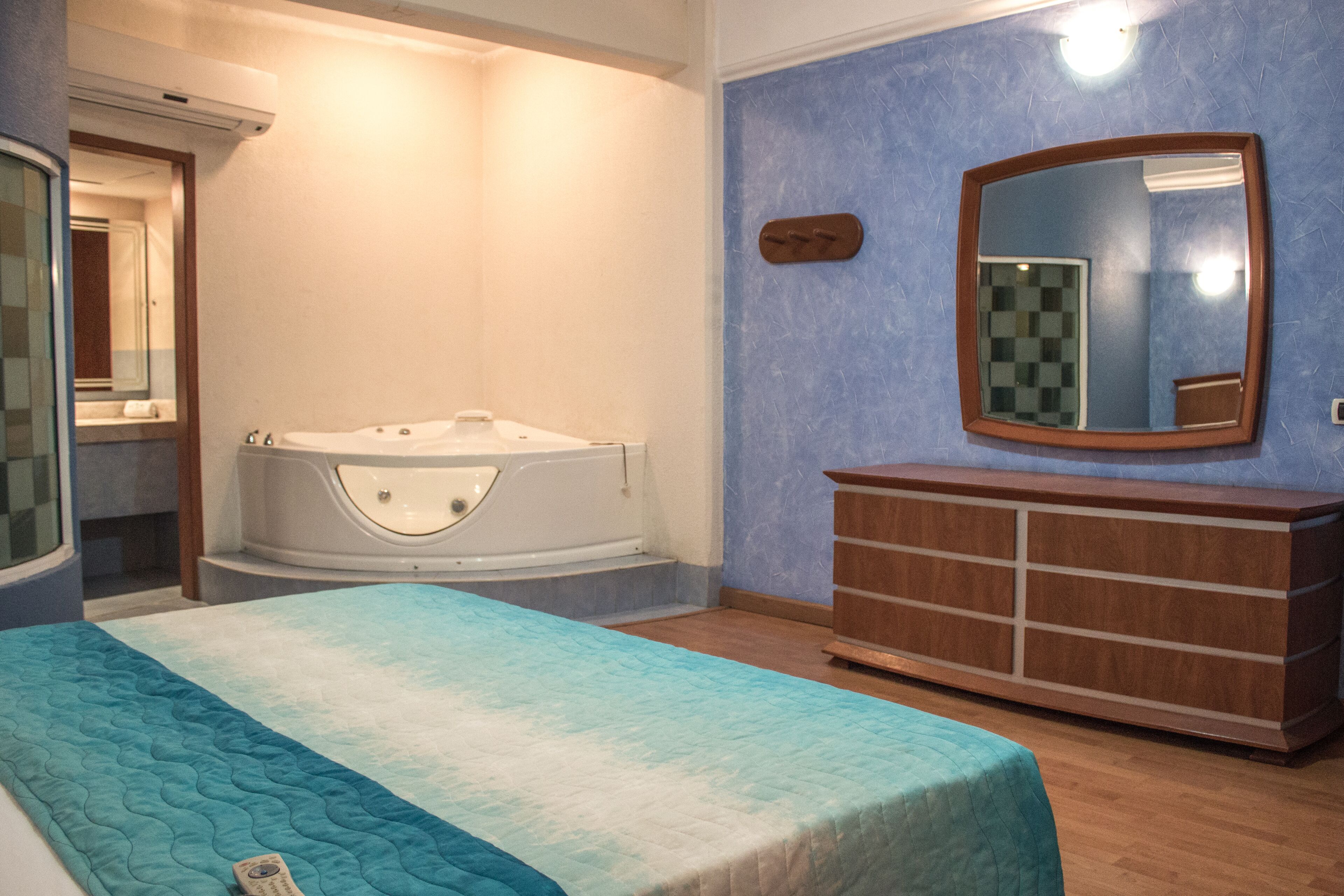 A bedroom with a bed, a wooden dresser, a large mirror, and a bathtub.
